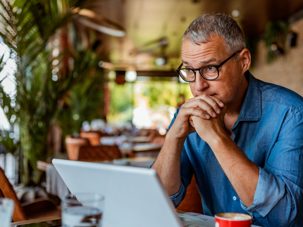 Contemplating businessman in the restaurant feeling sad. Full concentration on work. Confident mature man working on laptop while sitting at his working place in office. Tired manager sitting in restaurant surrounded with coffee and laptop computer having tired look , having pain, being sleepy and exhausted. Tiredness.