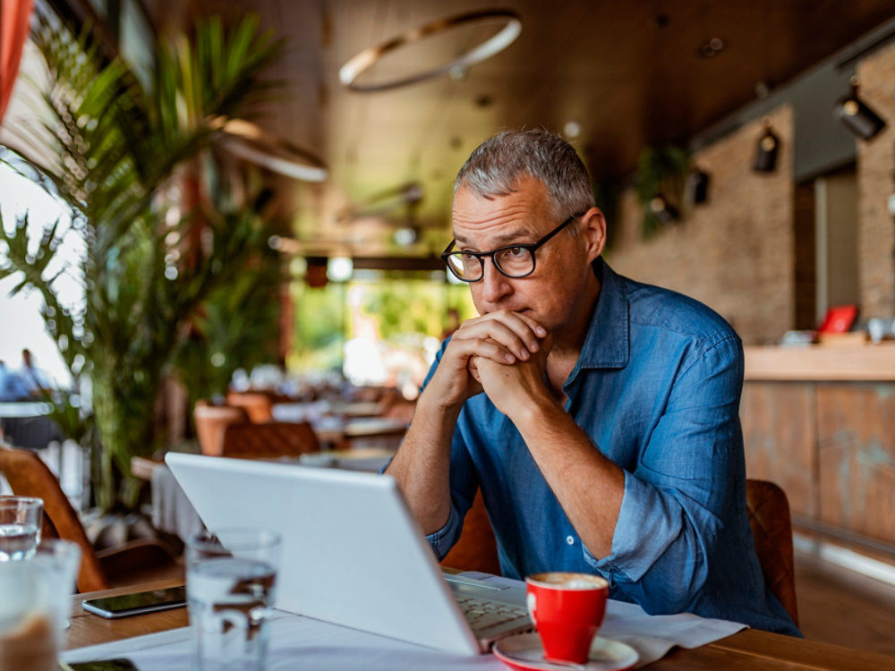 Contemplating businessman in the restaurant feeling sad. Full concentration on work. Confident mature man working on laptop while sitting at his working place in office. Tired manager sitting in restaurant surrounded with coffee and laptop computer having tired look , having pain, being sleepy and exhausted. Tiredness.