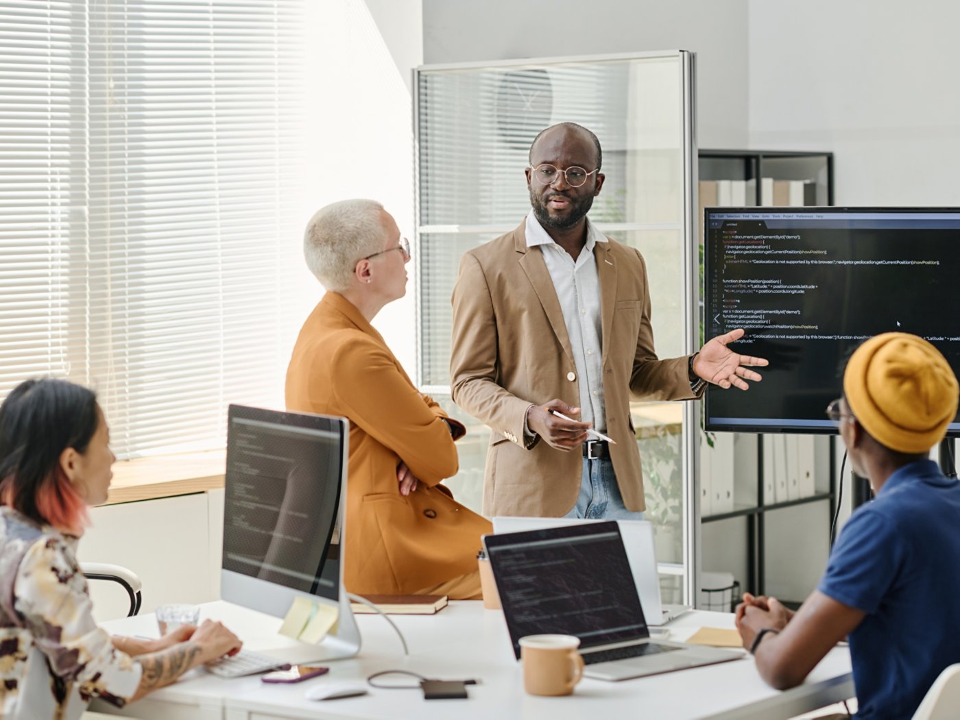 African businessman standing near the screen with presentation and presenting new software to programmers at meeting