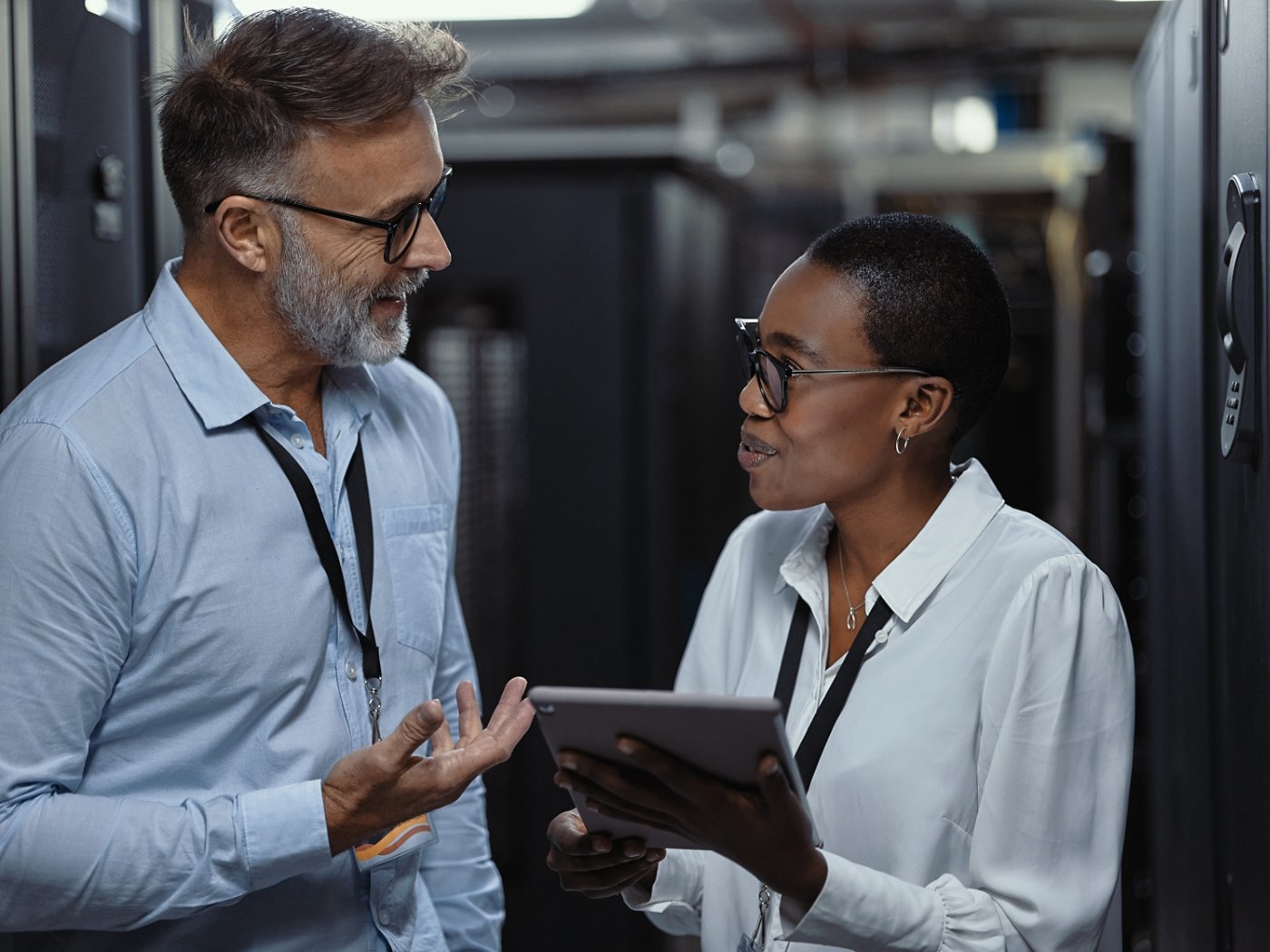 Two IT technicians using a digital tablet in a server room. Programmers fixing a computer system and network while doing maintenance in a datacenter. Happy engineers discussing successful solutions