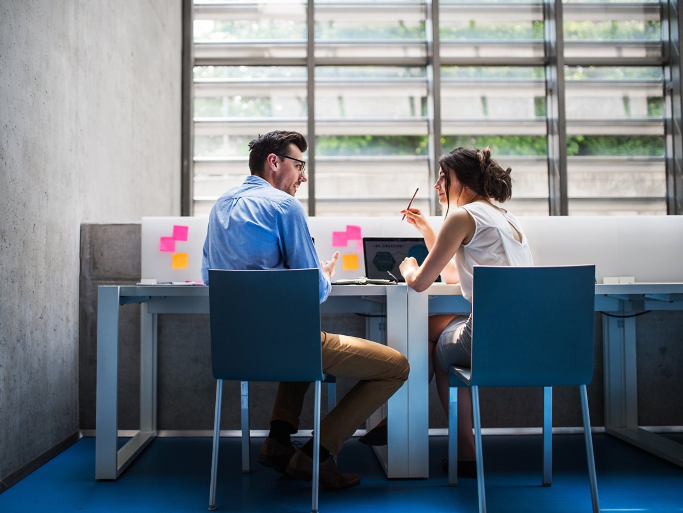 An attractive woman indoors talking to a handsome man sitting at the desk, discussing an issue.