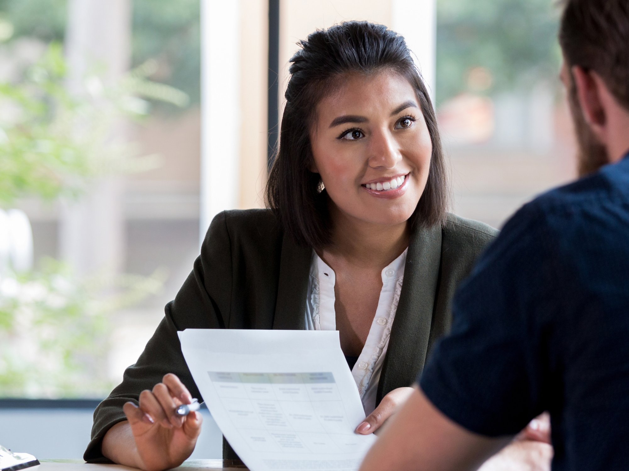 Hispanic businesswoman smiles while showing a document to a male associate.
