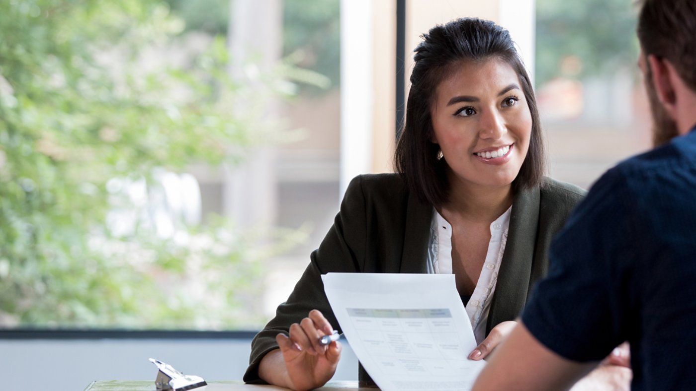 Hispanic businesswoman smiles while showing a document to a male associate.