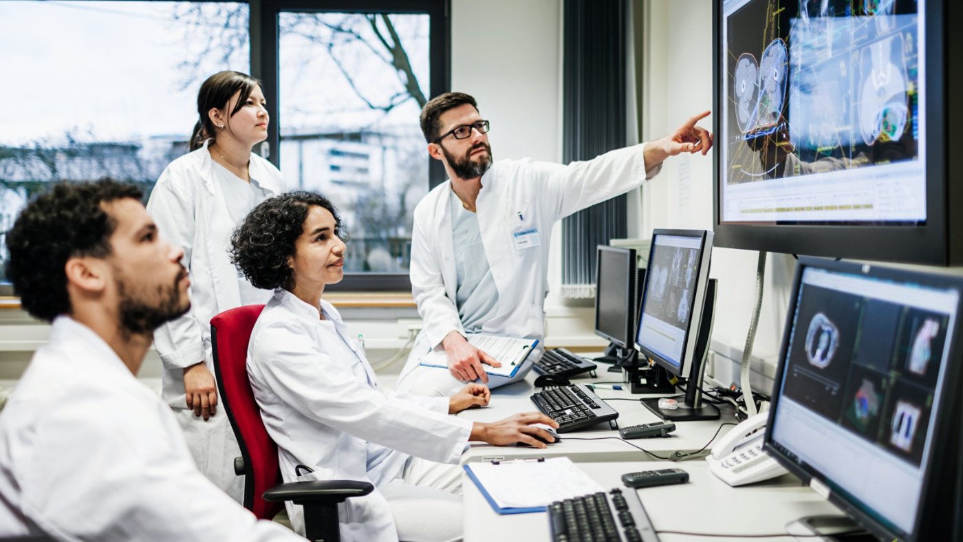 A team of doctors looking at some lab results together on monitors, in an office at the hospital.