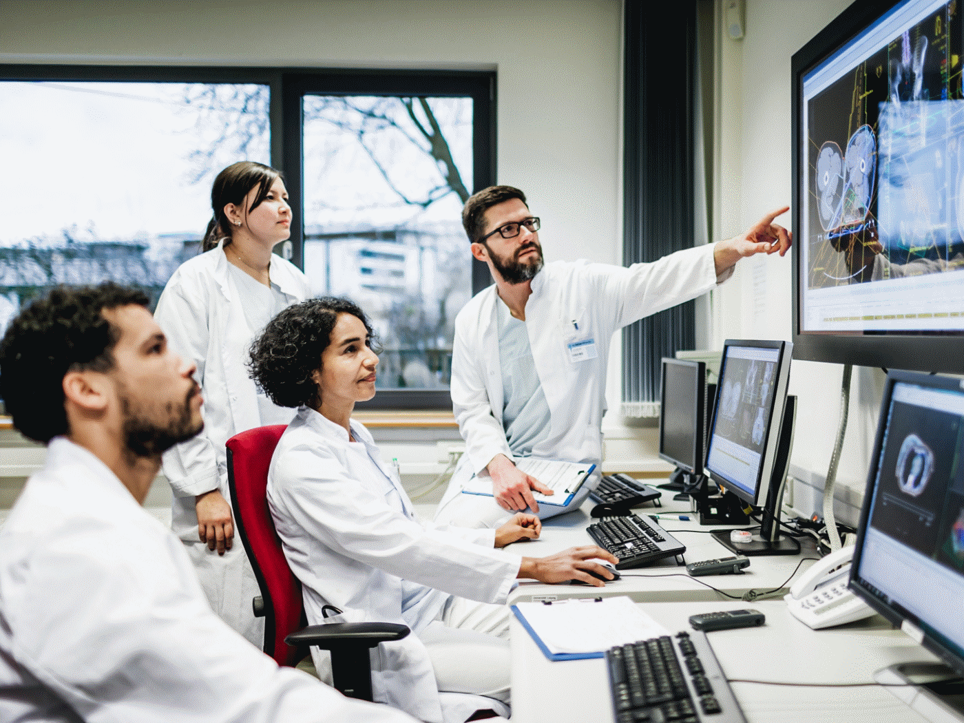 A team of doctors looking at some lab results together on monitors, in an office at the hospital.