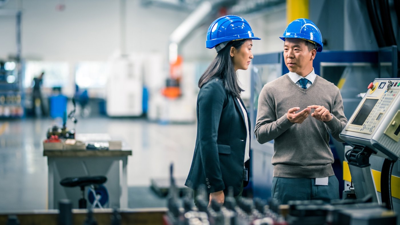 Manager and engineer discussing while examining control panel in factory.