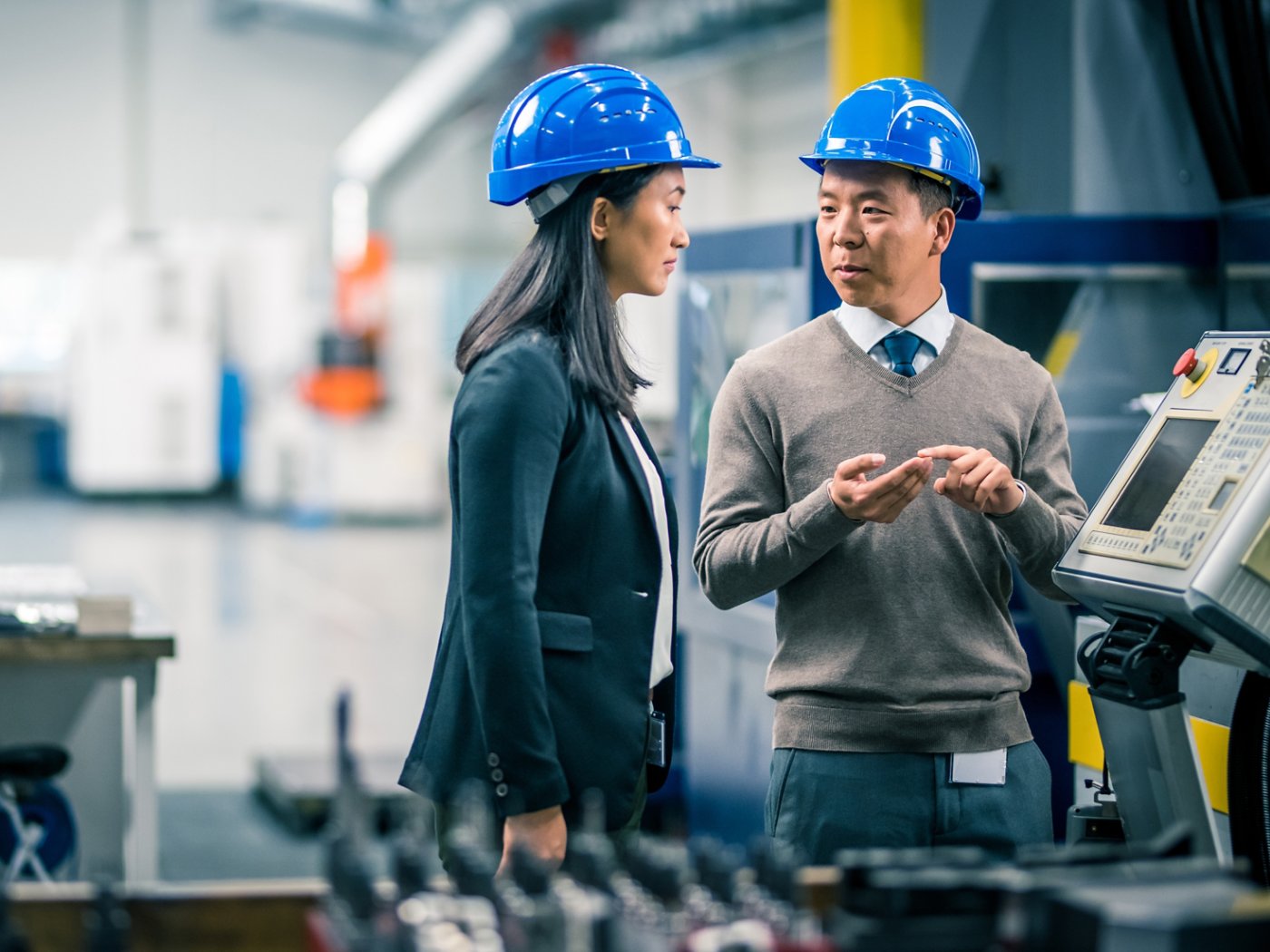 Manager and engineer discussing while examining control panel in factory.