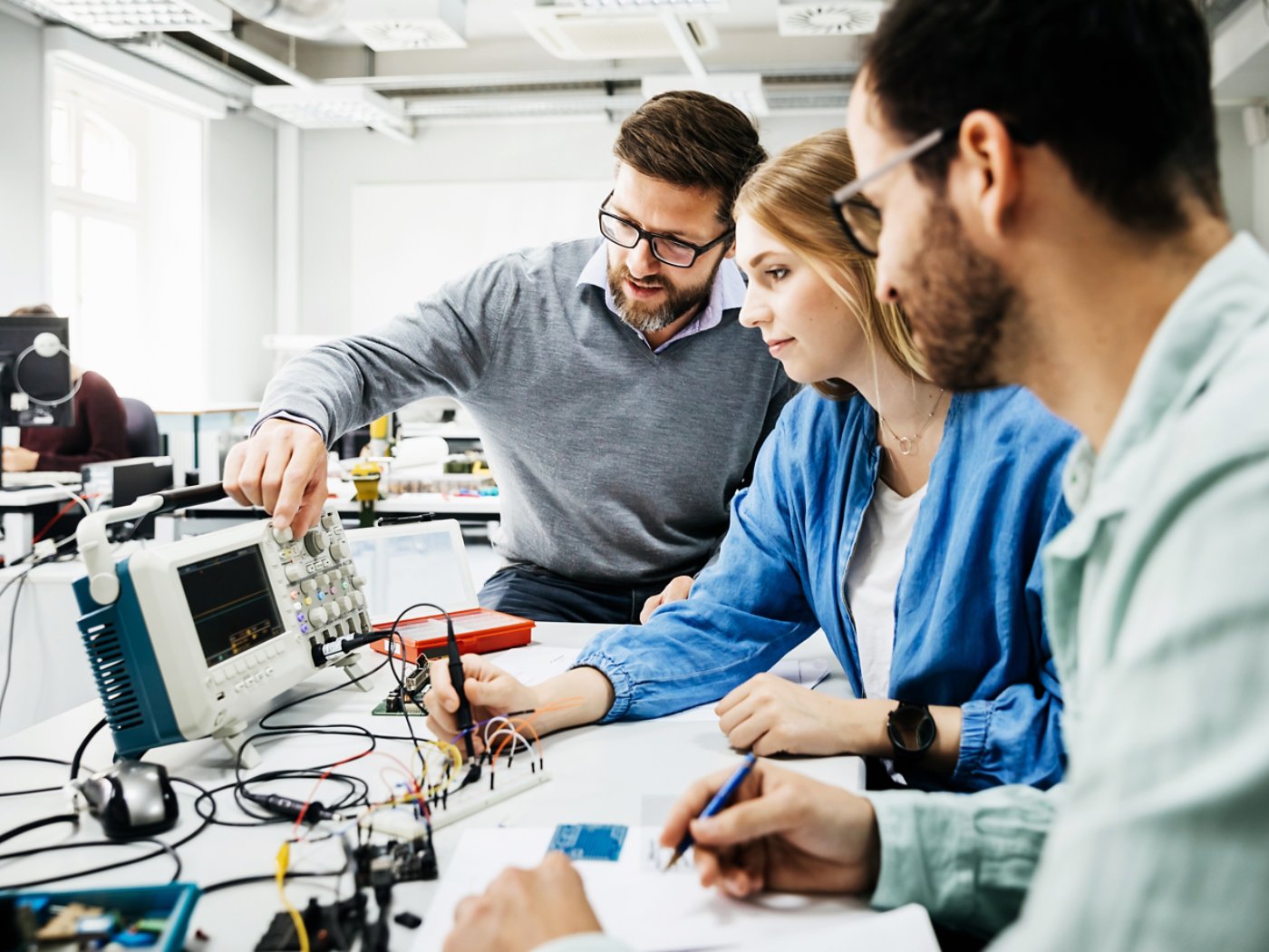 An engineering tutor showing his students how to use some electronic equipment during a teaching session at university.