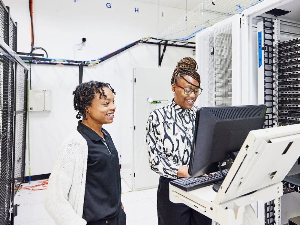 Medium wide shot of smiling female IT professionals in discussion while configuring server in data center