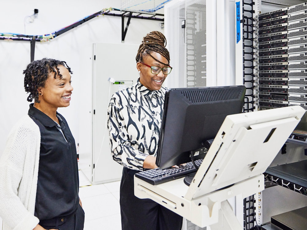 Medium wide shot of smiling female IT professionals in discussion while configuring server in data center