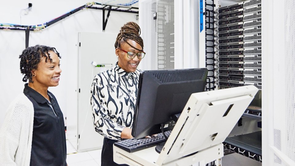 Medium wide shot of smiling female IT professionals in discussion while configuring server in data center