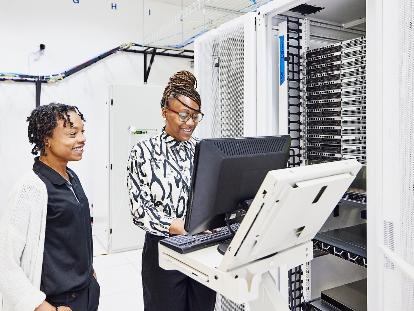 Medium wide shot of smiling female IT professionals in discussion while configuring server in data center