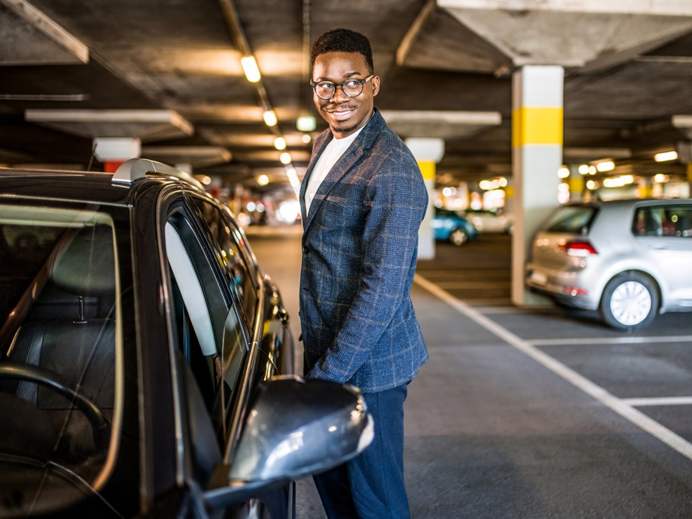 Cheerful African American entrepreneur getting in his car at public car garage.