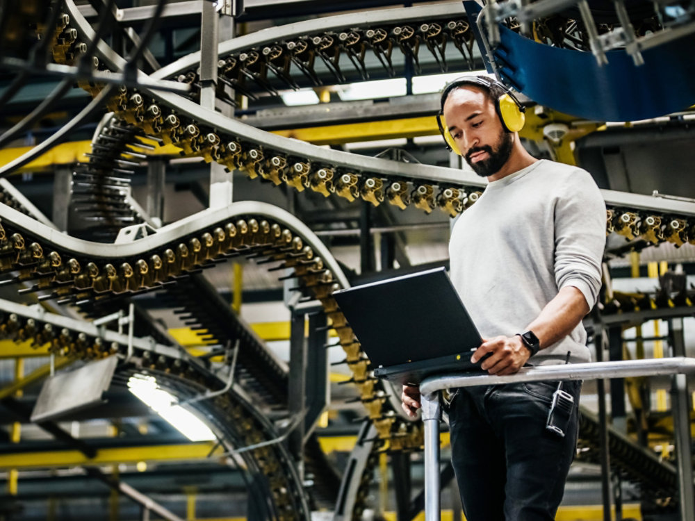 A print factory engineer standing alongside a variety of moving rails and machinery.