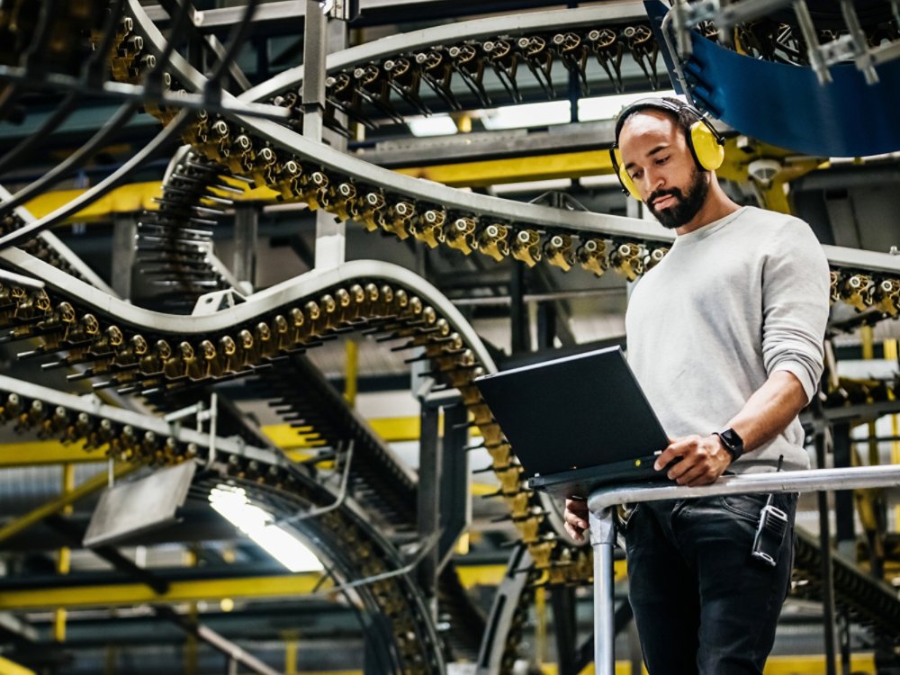 A print factory engineer standing alongside a variety of moving rails and machinery.