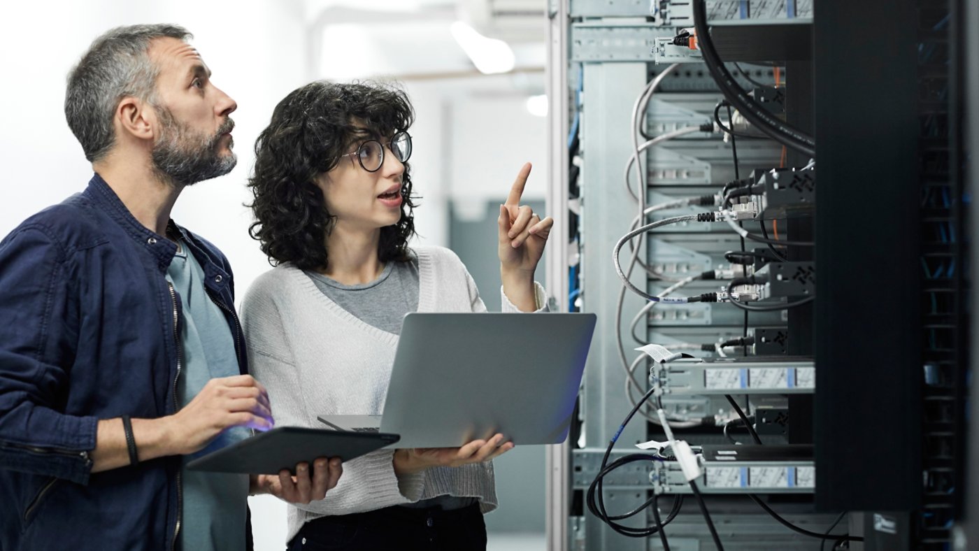 Female technician guiding male about cables. Engineer with digital tablet talking to coworker at workplace. They are in server room.