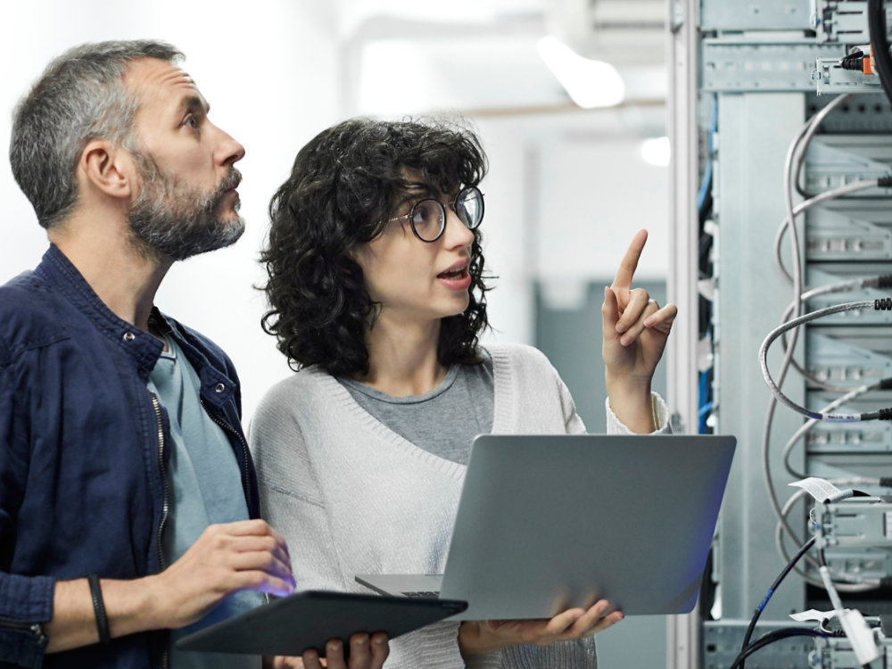 Female technician guiding male about cables. Engineer with digital tablet talking to coworker at workplace. They are in server room.