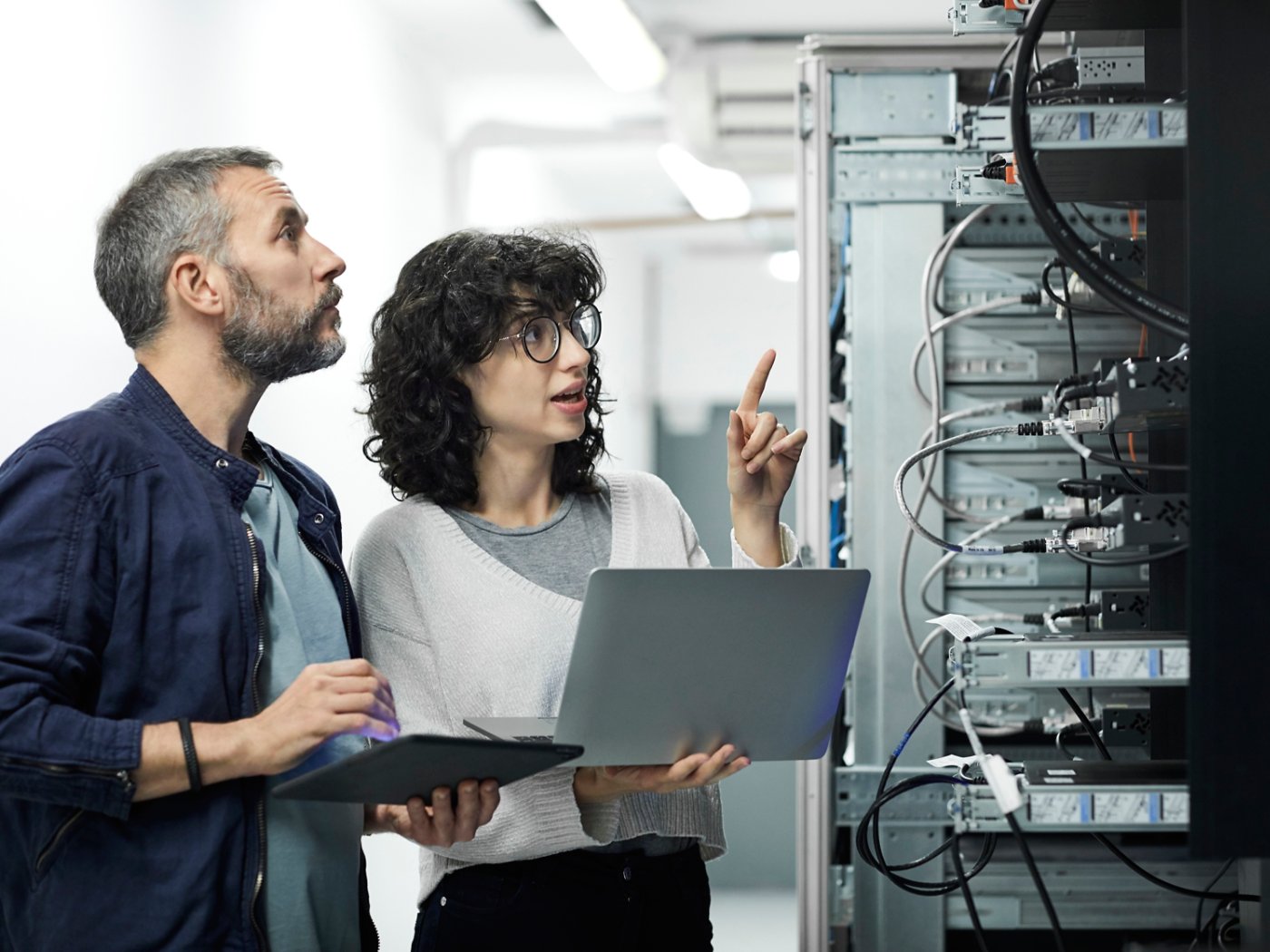 Female technician guiding male about cables. Engineer with digital tablet talking to coworker at workplace. They are in server room.