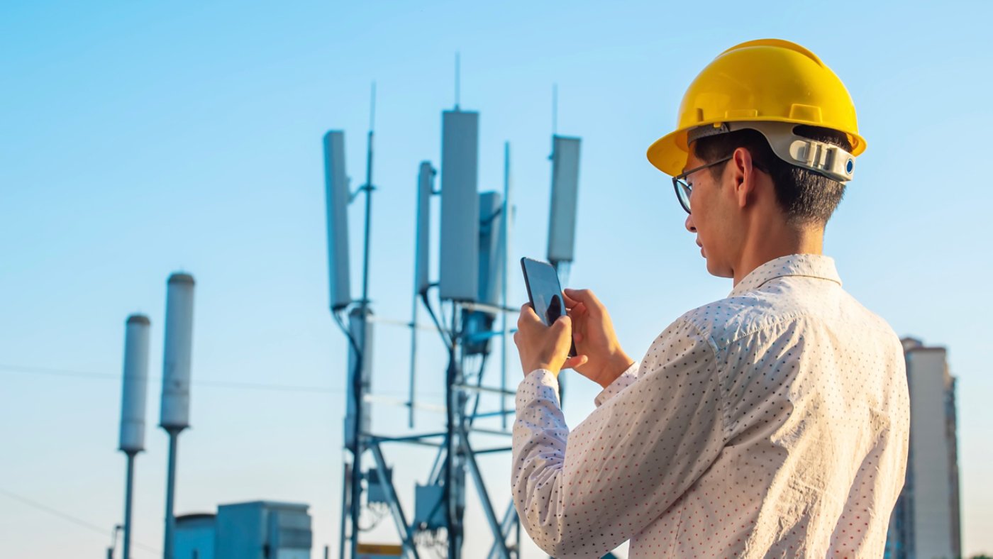 Engineer holding mobile phone testing the communications tower