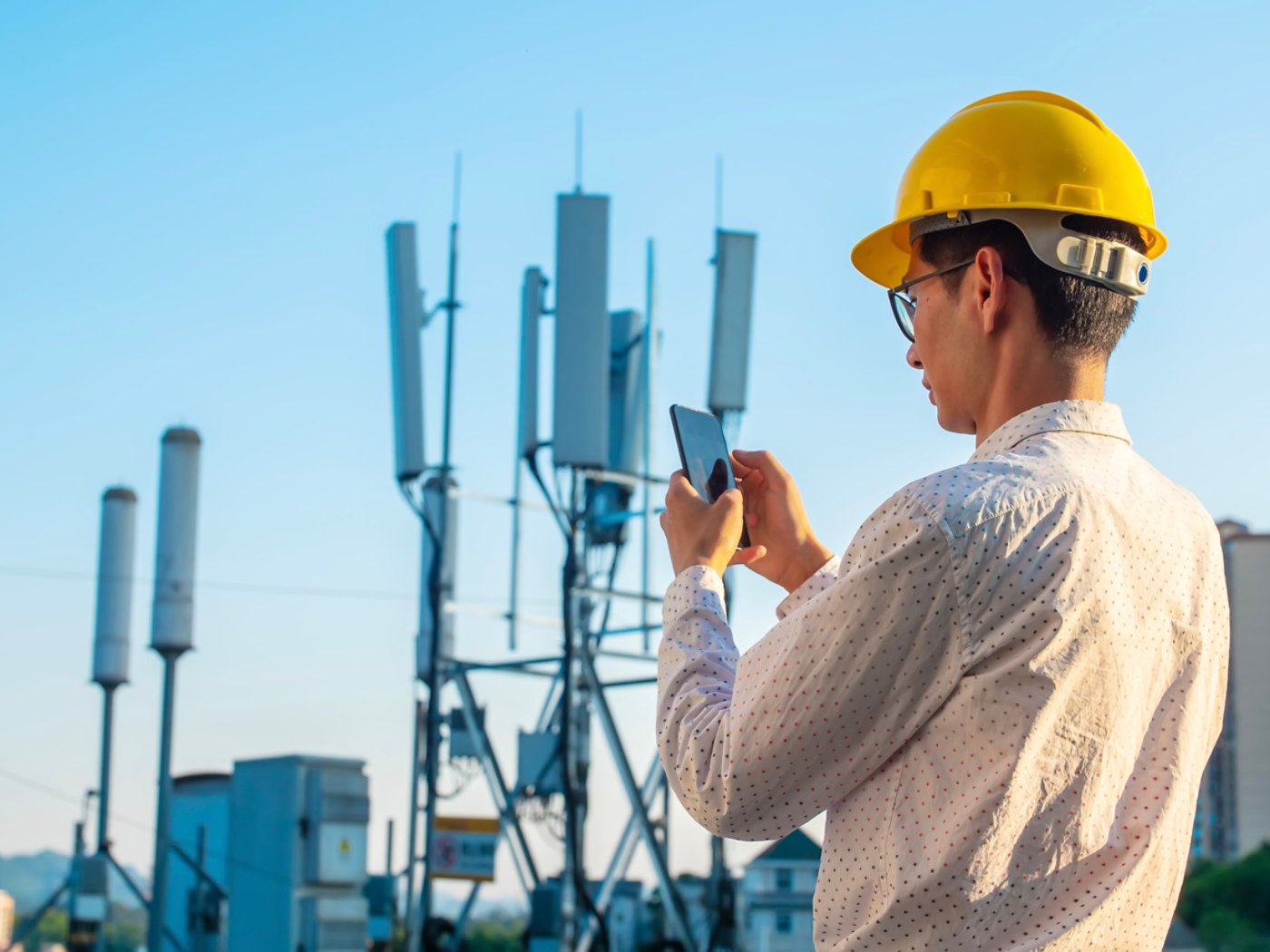 Engineer holding mobile phone testing the communications tower
