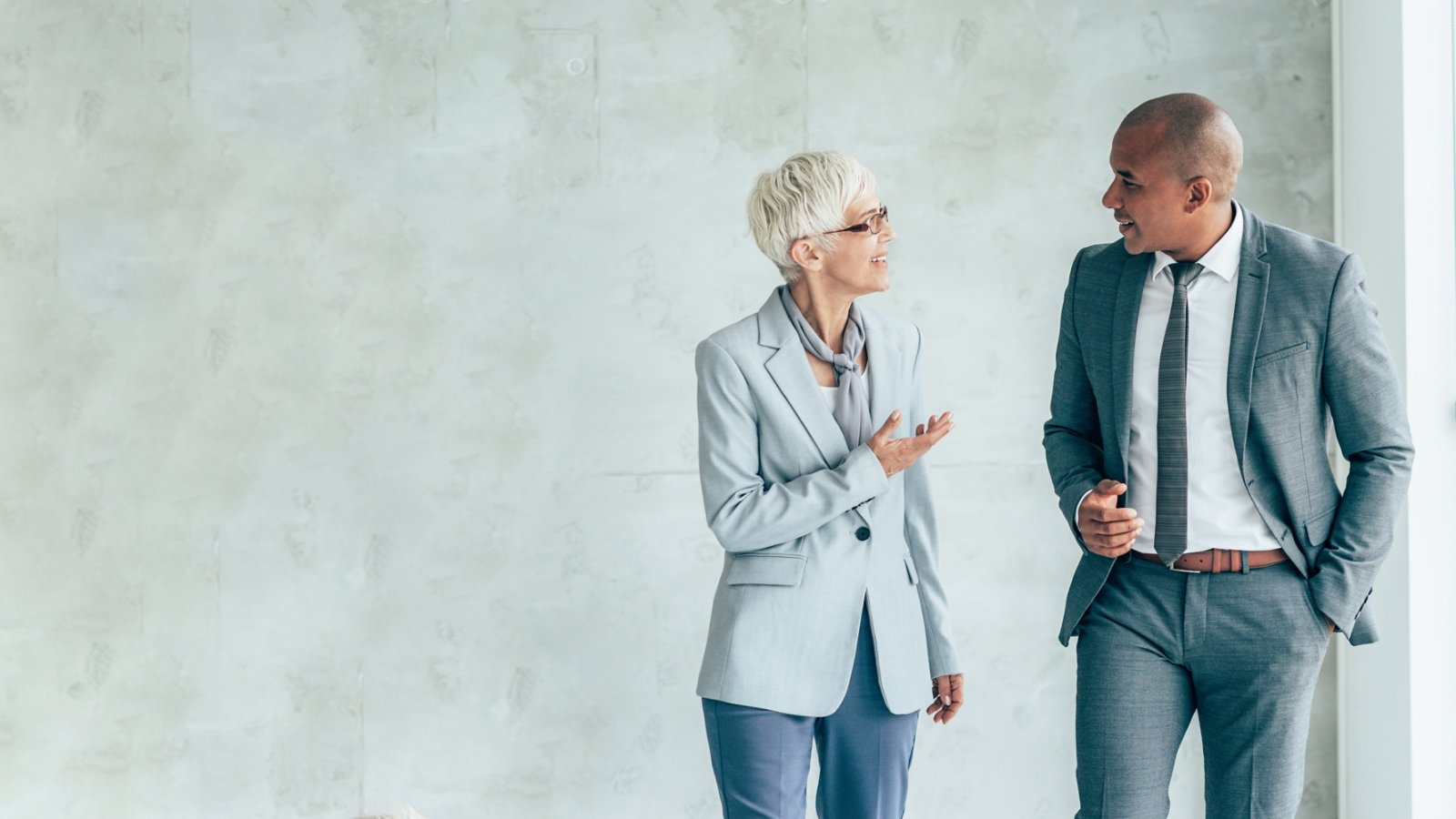 Two smiling business people walking through office hall and talking