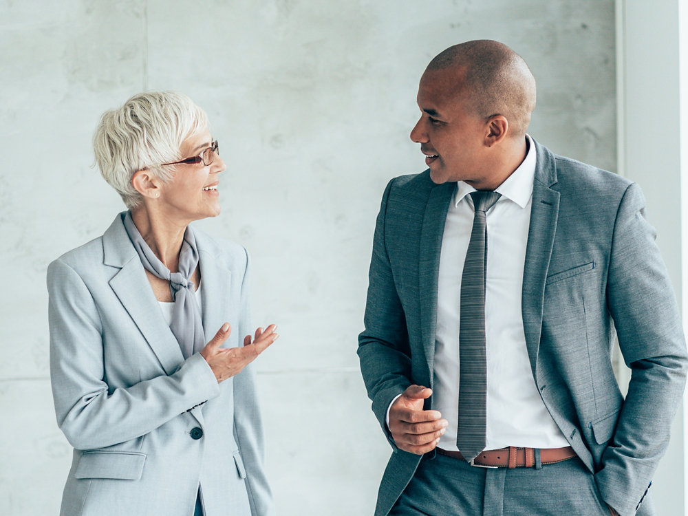 Two smiling business people walking through office hall and talking