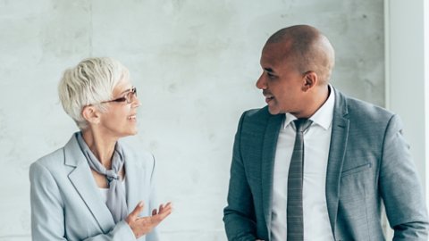 Two smiling business people walking through office hall and talking