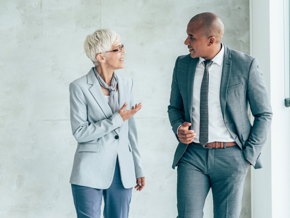 Two smiling business people walking through office hall and talking