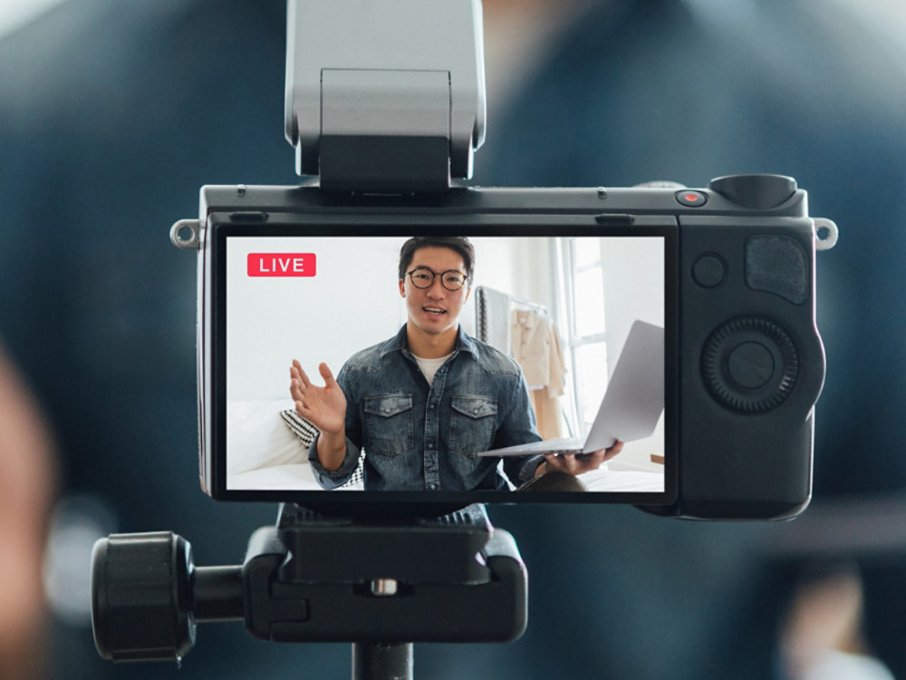 Copped shot of confident young man talking while filming through video camera for vlogging at home.