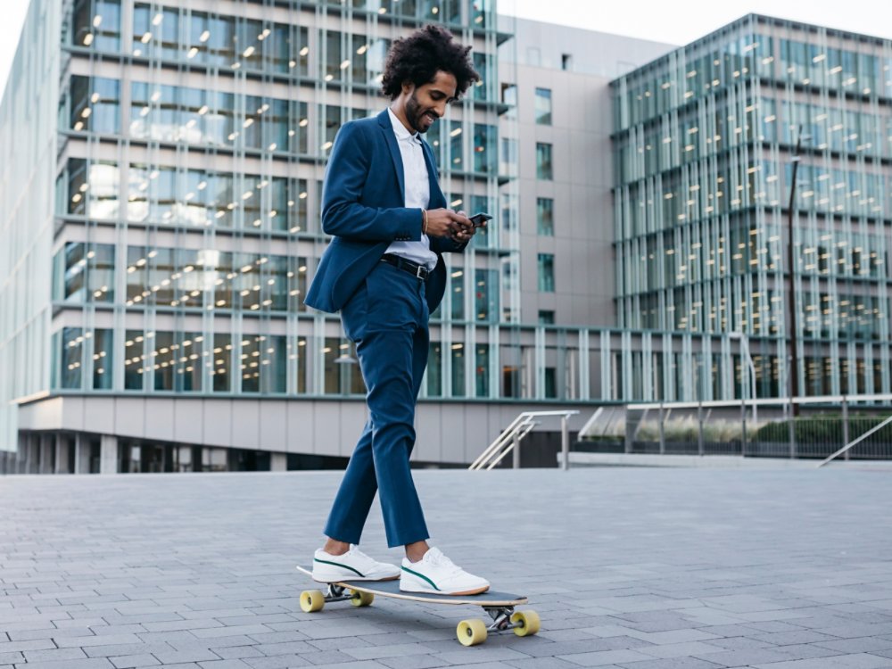 Spain, Barcelona, young businessman riding skateboard and using cell phone in the city