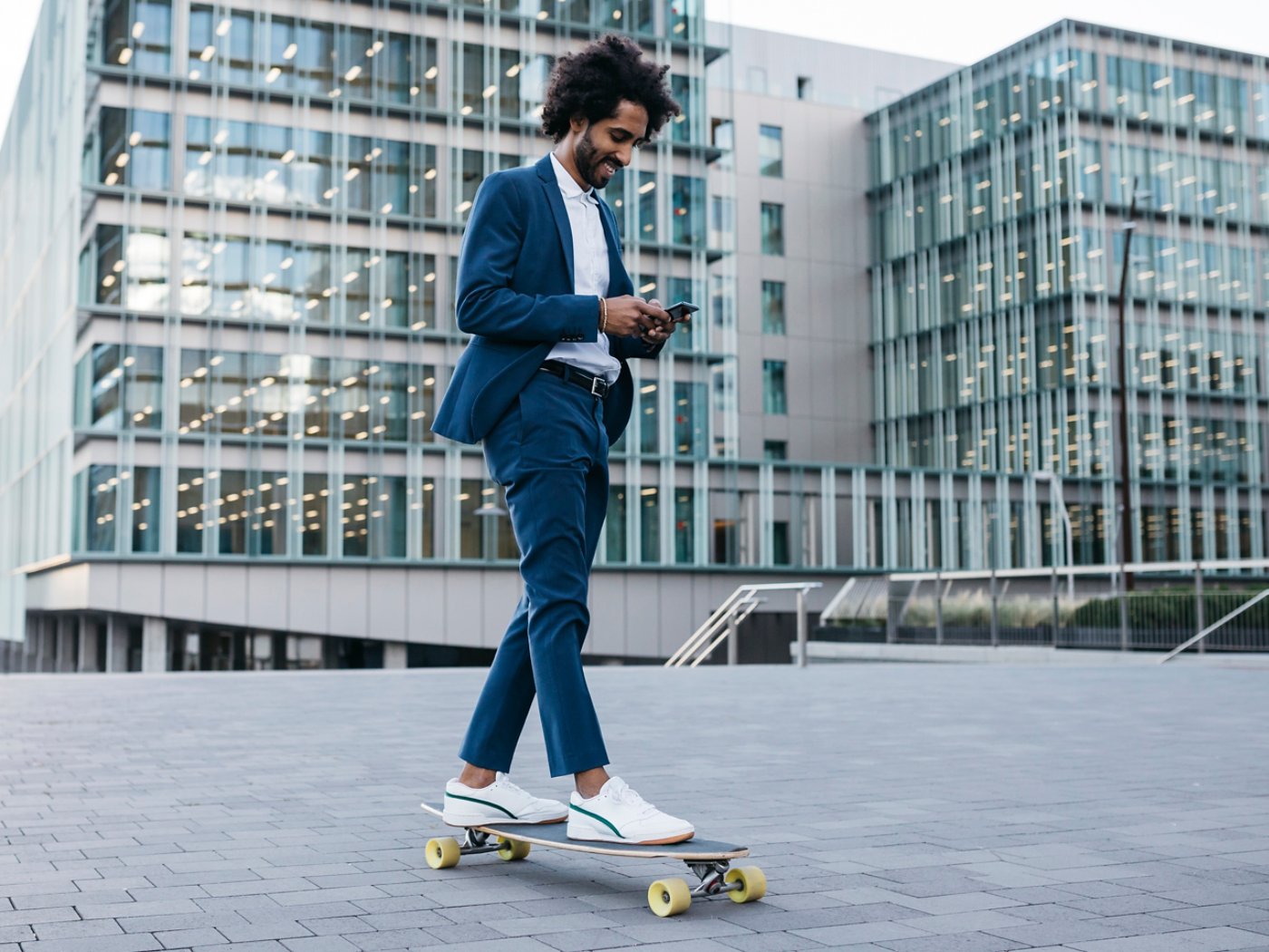 Spain, Barcelona, young businessman riding skateboard and using cell phone in the city