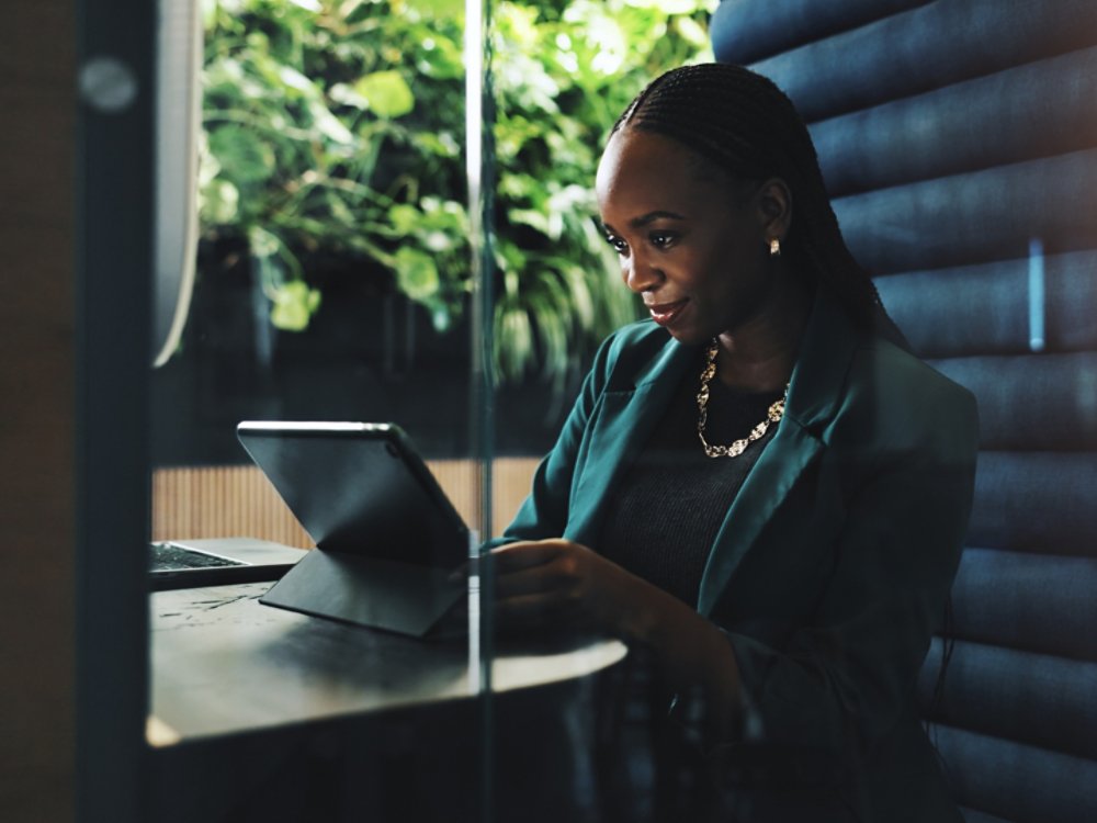 Tablet, office and businesswoman in cubicle for company budget review and accounting news. Technology, hybrid work booth and African financial manager with online investment report or reading update.