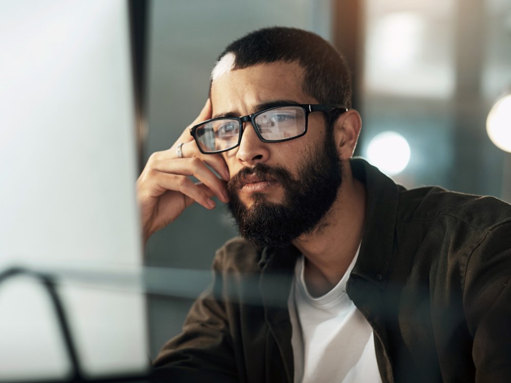 The later it gets the deeper he goes. Shot of a young businessman using a computer during a late night in a modern office.