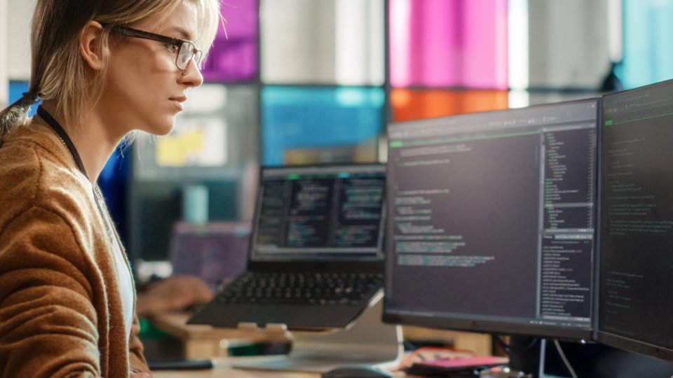 Caucasian Woman Coding on Desktop PC and Laptop Setup With Multiple Displays in Spacious Office. Female Junior Software Engineer Working on New Sprint of Mobile Application Development For Start-up.