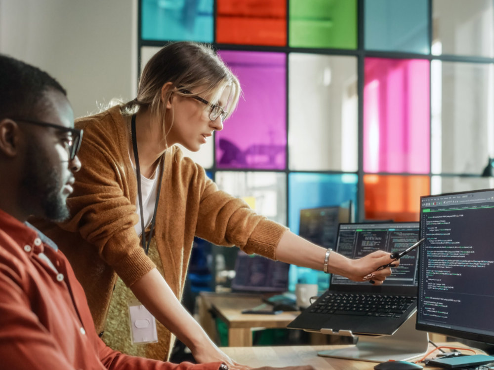 African American Software Engineer Shows Code on Desktop Computer to Female Project Manager in Stylish Office. Black Man And Caucasian Woman Discussing Progress of AI Application Development., African American Software Engineer Shows Code on Desktop Compute