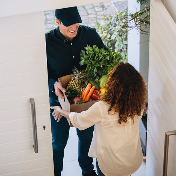 High angle view of a female customer receiving groceries from delivery man at the house's door. Delivery employee delivering a box of fruits and vegetables to a woman.