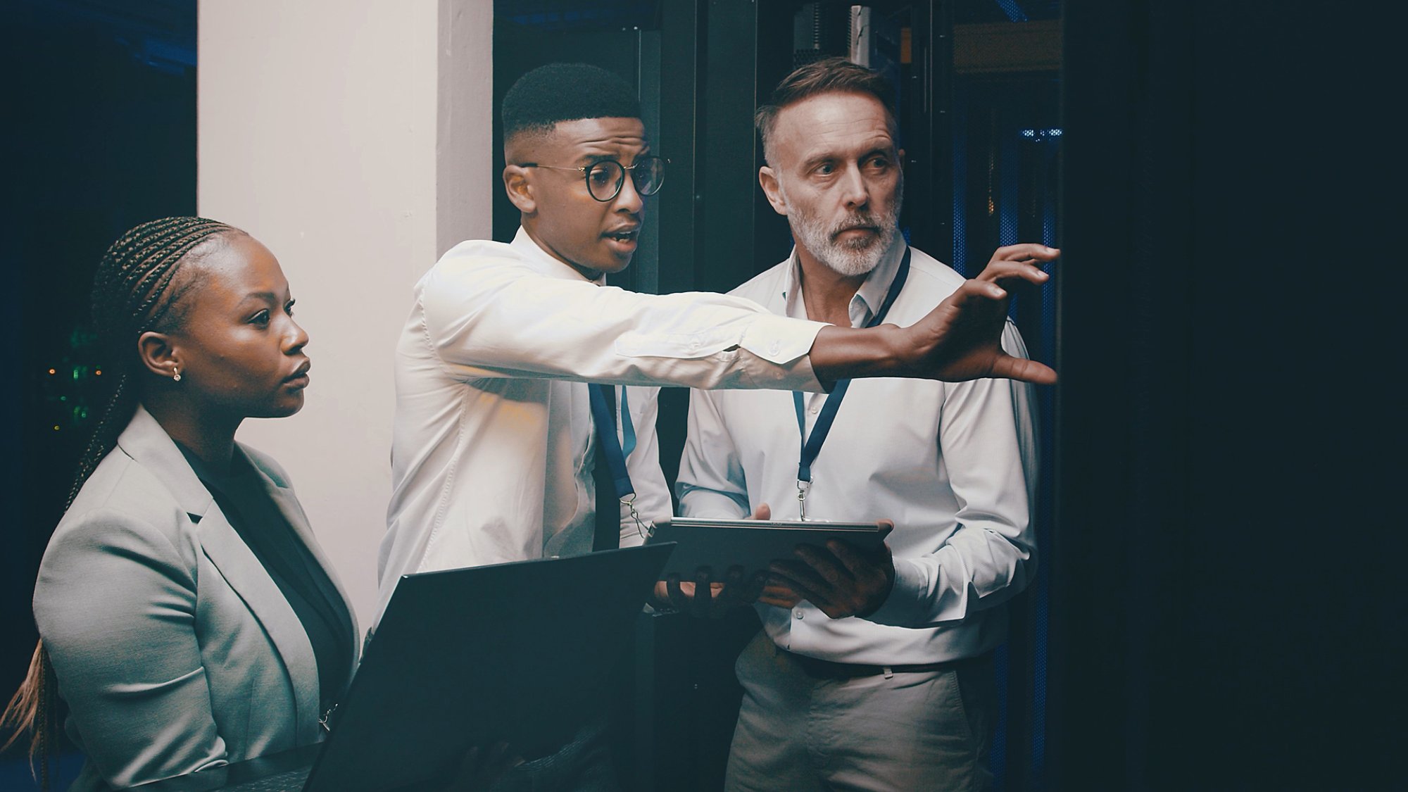 Man, tablet and group with discussion in server room with cybersecurity, system and hardware check. Programmer, tech and team with app for software update, assessment and IT solution at data center.