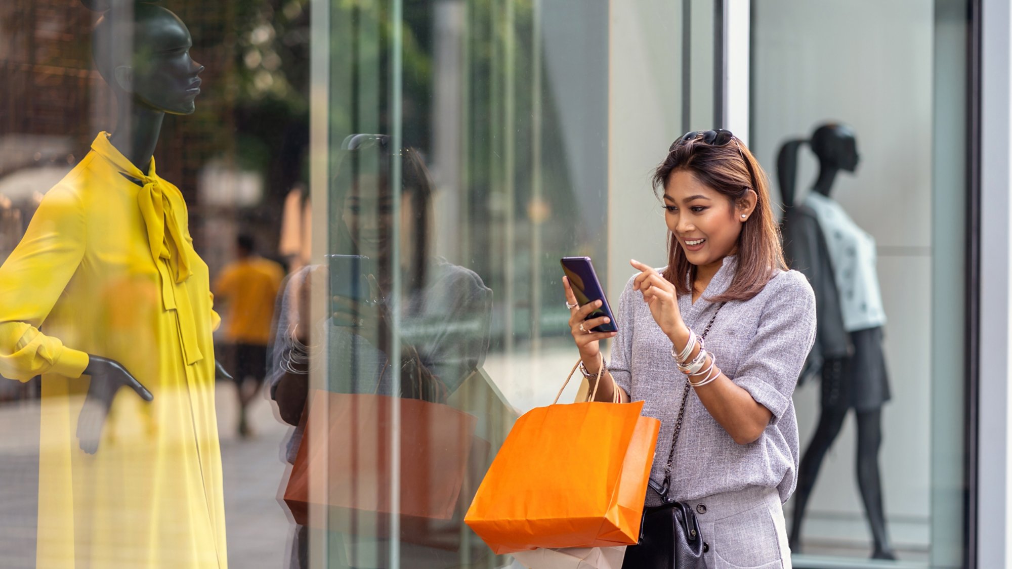 Asian woman using the smart mobile phone for check online shopping order is completed with clothes beside the glassess in store shop with happy action at department center