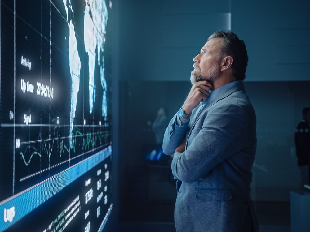Senior Computer Science Engineer Looking at Big Screen Display Showing Global Map with Data Points. Telecommunications Technology Company System Control and Monitoring Room with Servers.