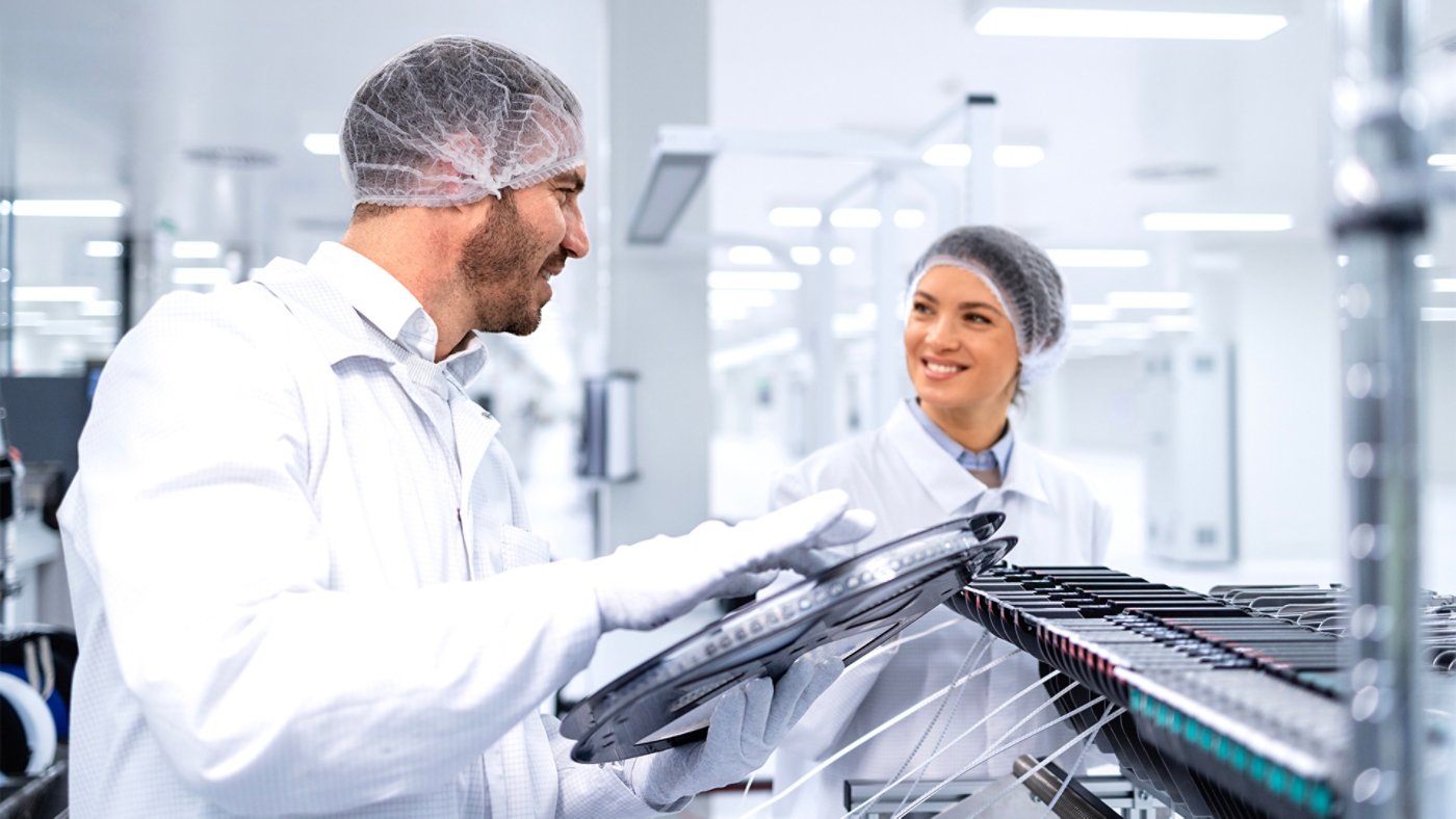 Factory workers operating advanced semiconductor production machine in automotive industry.