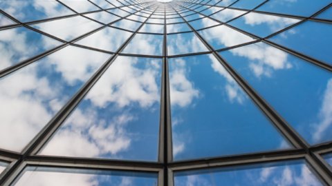 Blue sky and white clouds reflecting in a curved glass building