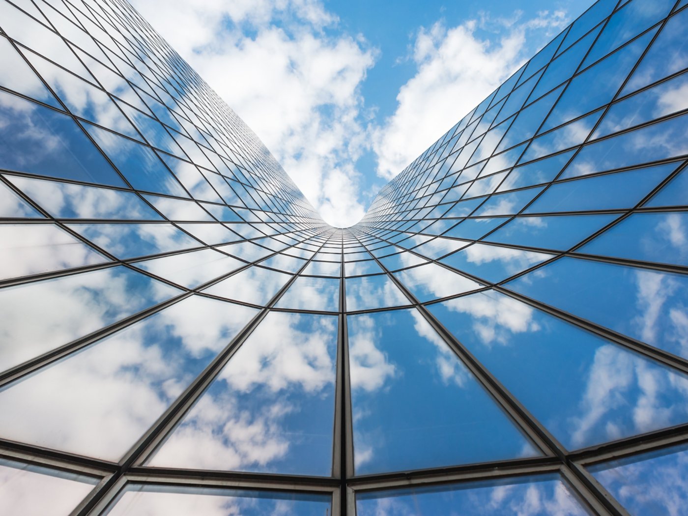 Blue sky and white clouds reflecting in a curved glass building