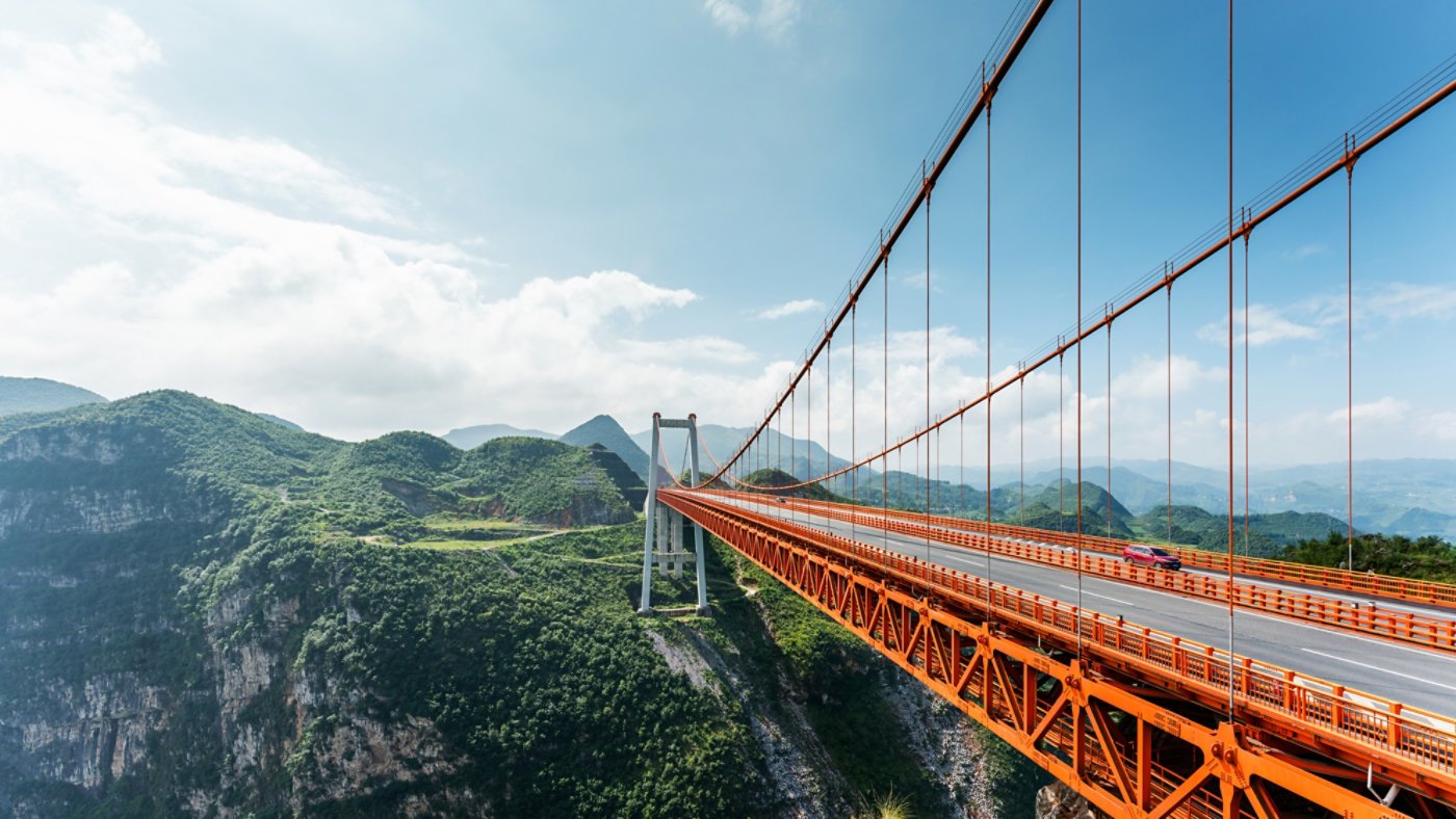 Red suspension bridge leading into a mountain