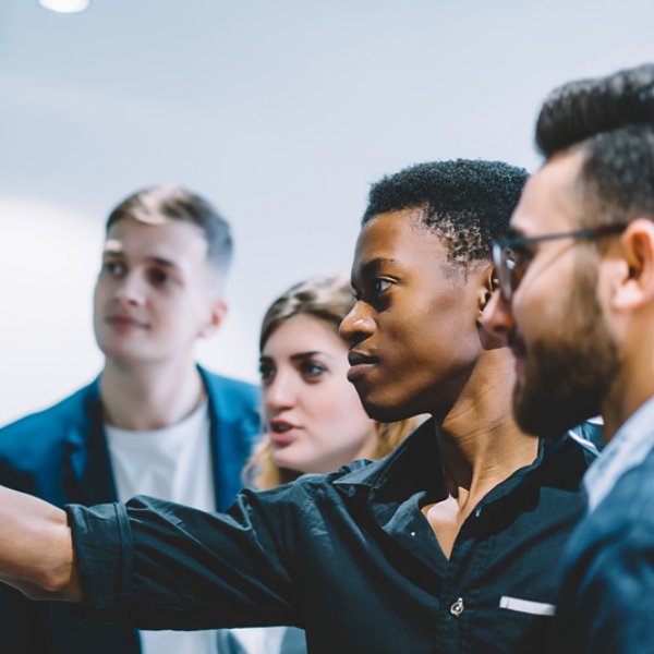 Diverse team of skilled students together solving task writing down information on papers glued on wall.Multicultural young people collaborating on business plan making notes of ideas on sticker