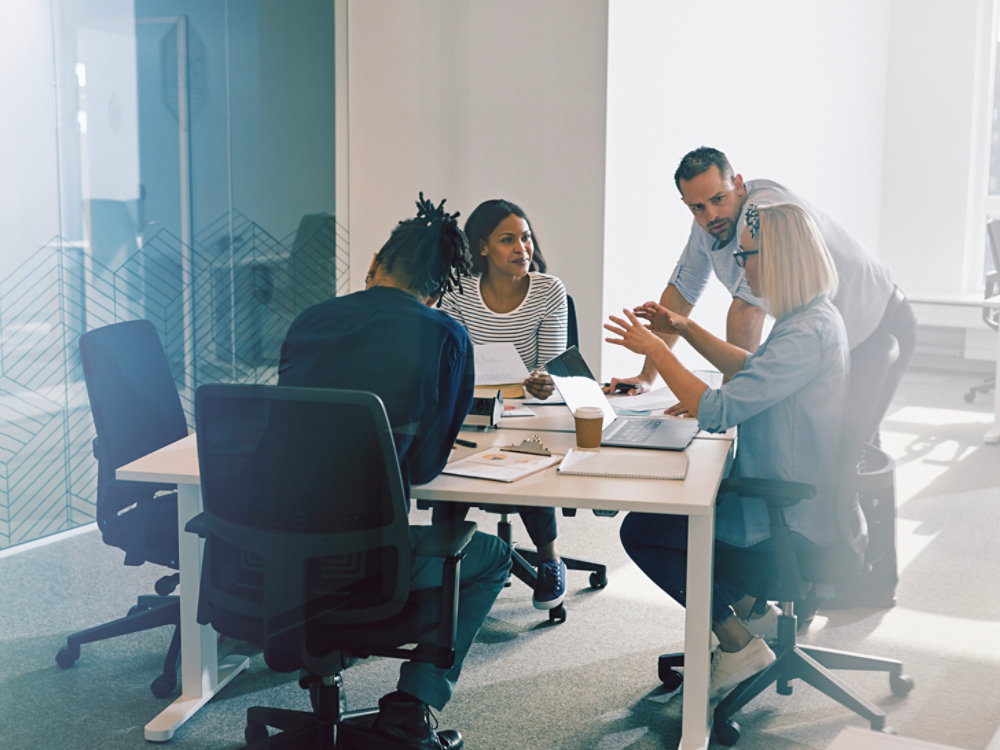 Focused group of diverse work colleagues talking business together during a meeting around a table inside of a glass walled office