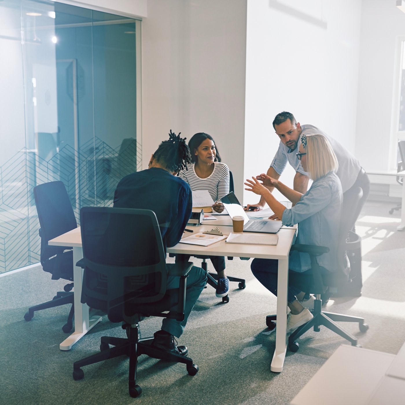 Focused group of diverse work colleagues talking business together during a meeting around a table inside of a glass walled office