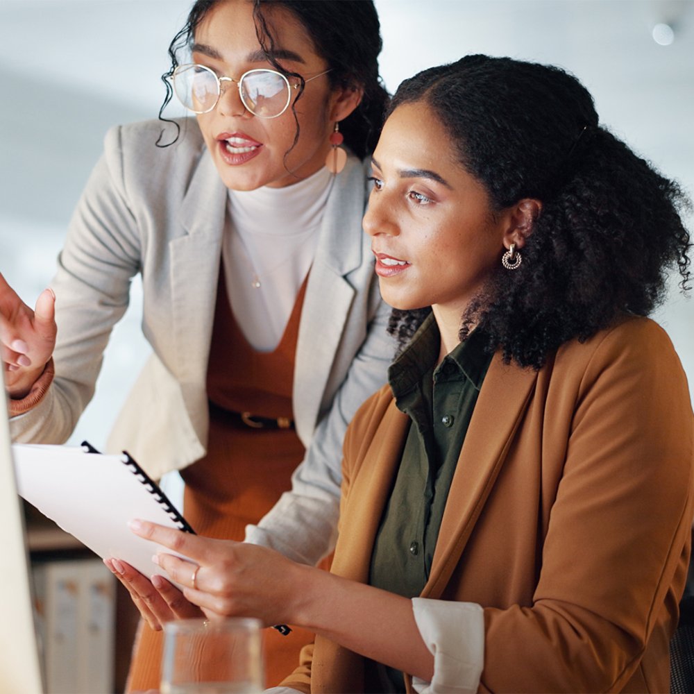 Communication, coaching and women in business with documents for training and project management on laptop. Instruction, mentor or leader talking to colleague with paperwork for report in office.