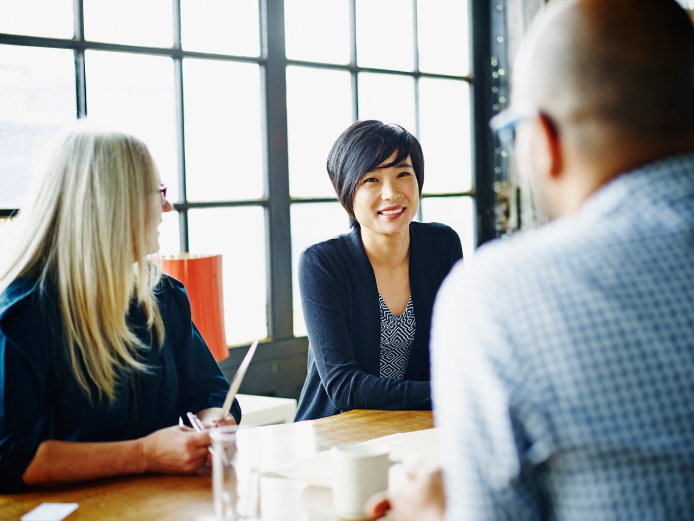 Smiling businesswoman leading discussion with colleagues during meeting at office conference table 4X3