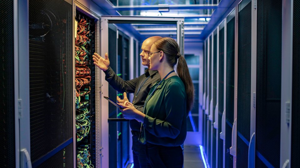 Side view of a man and a woman talking about a server in a data center while looking at it's network connection cables.