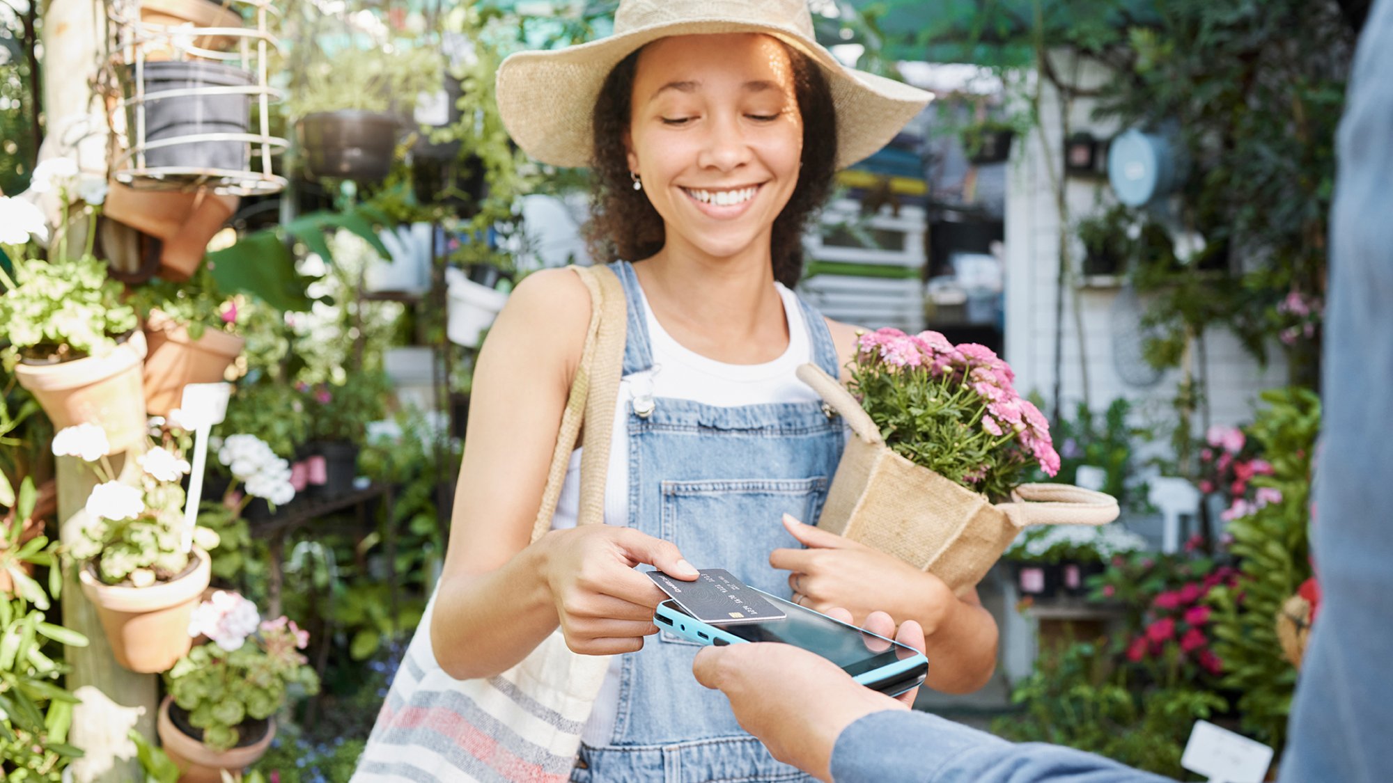 Payment, flower shopping and woman at a nursery, credit card tapping and machine for ecology at a small business. Paying, bouquet and girl buying flowers with a debit card at a shop for agriculture.